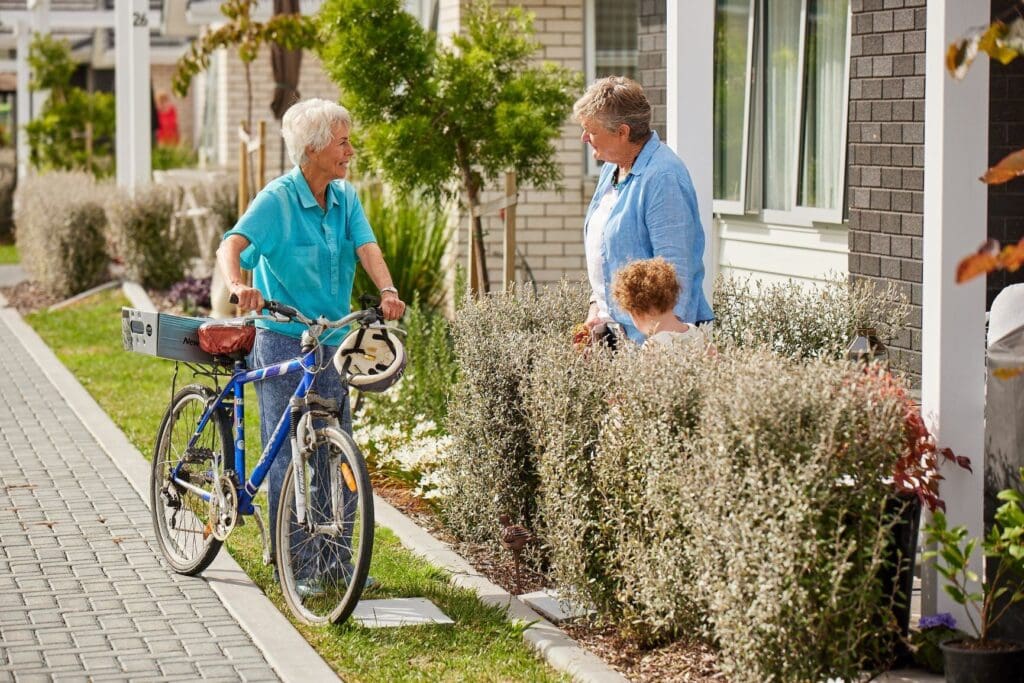 Image shows woman on bike delivering mail to a Karaka Pines Villages resident outside her home.